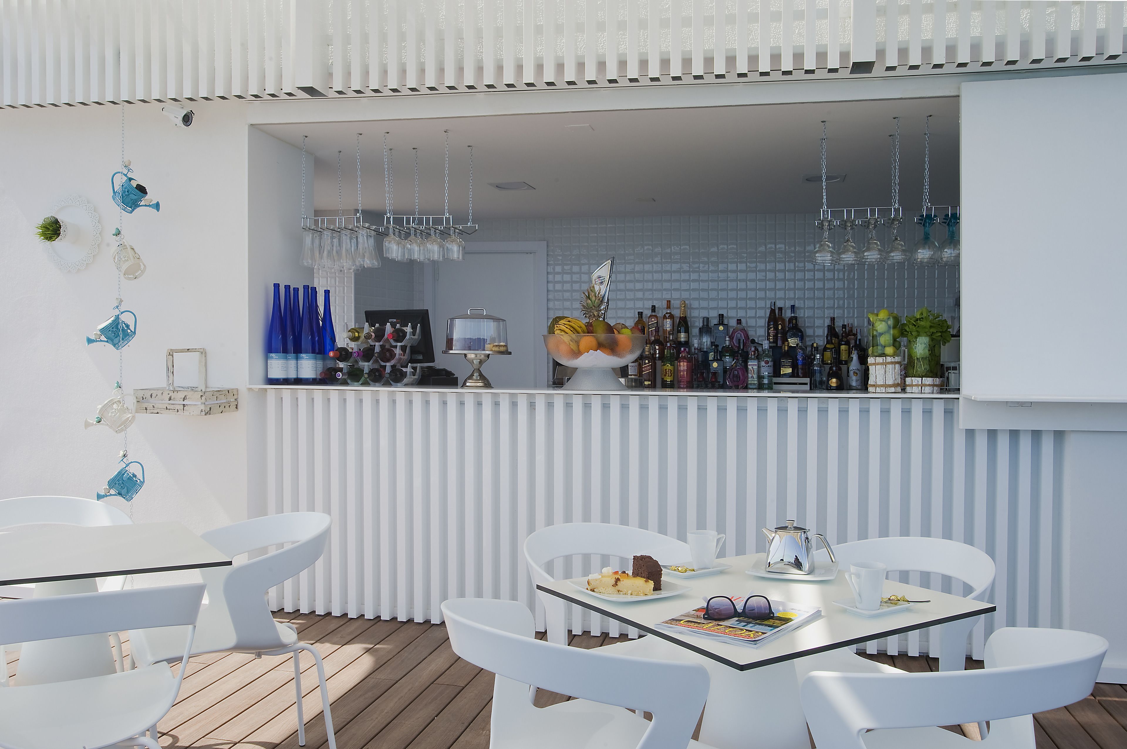 A modern outdoor bar area with white furniture, a variety of bottles, and a fruit bowl.