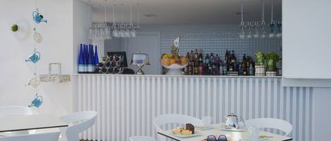 A modern outdoor bar area with white furniture, a variety of bottles, and a fruit bowl.