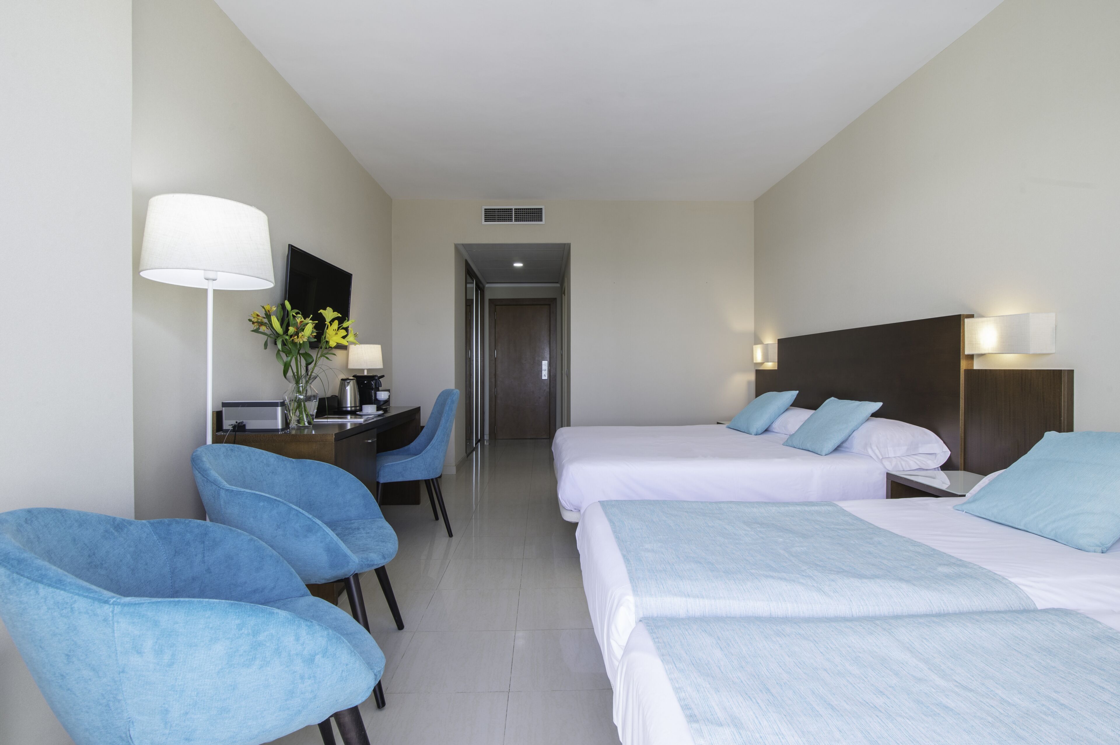 A hotel room with two beds, a desk with a chair, a lamp, and a mirror.