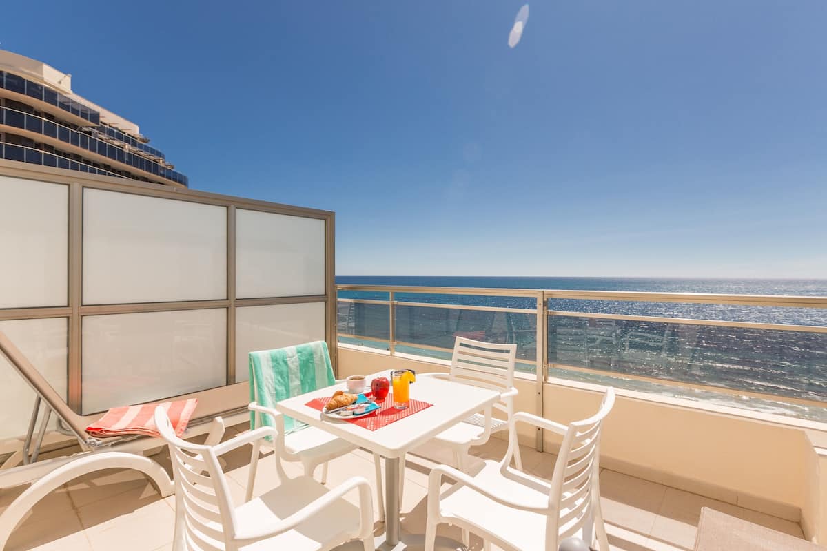 A balcony with a table set for breakfast, white chairs, and a view of the ocean.