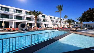 A hotel with a swimming pool, palm trees, and a modern building with balconies.