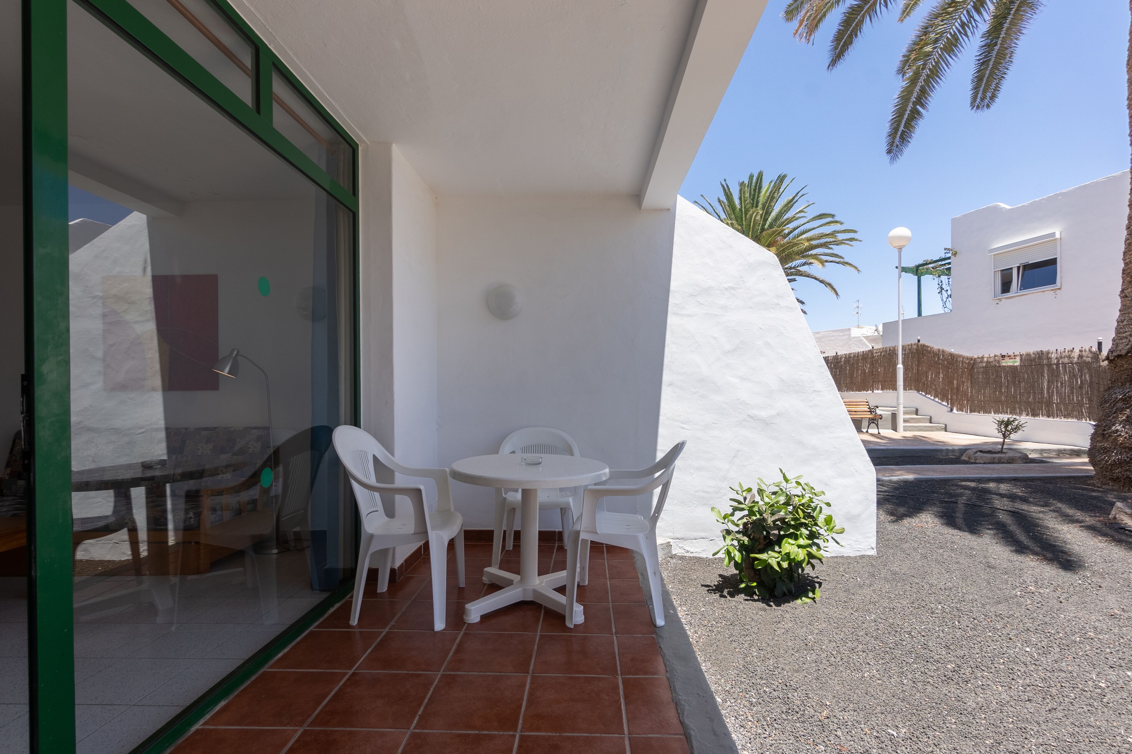 A patio with a table and chairs, a small plant, and a view of a white building and palm trees.