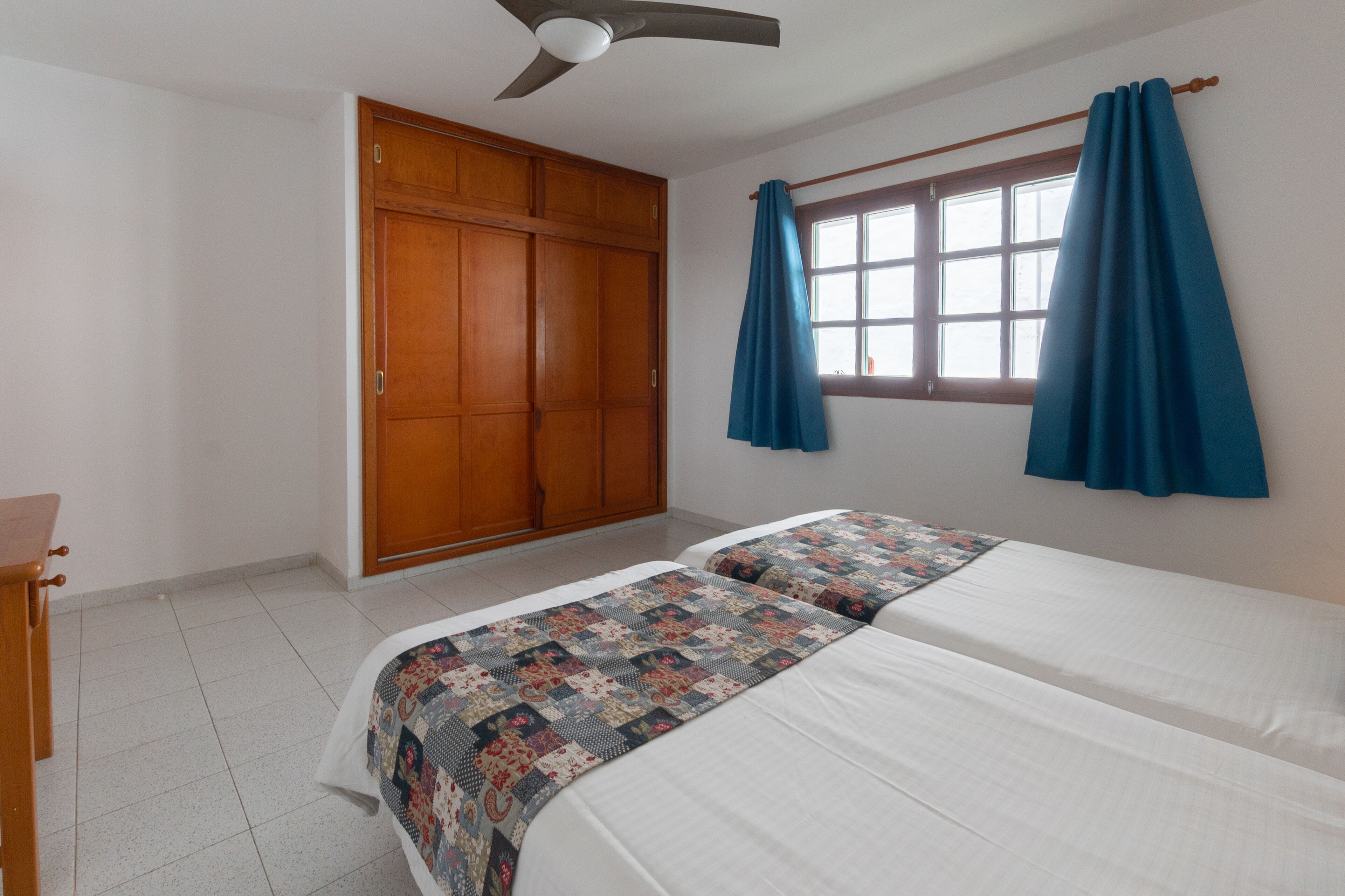 Un dormitorio con cama, armario, ventilador de techo y ventana con cortinas.