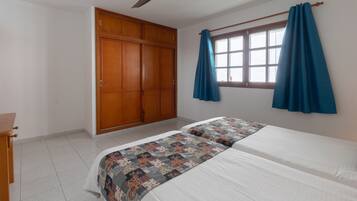 A bedroom with a bed, a wardrobe, a ceiling fan, and a window with curtains.