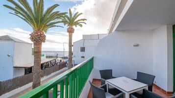 Un balcon doté de meubles en osier et de deux palmiers, donnant sur une plage.