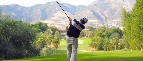 A golfer on a golf course with a mountainous backdrop.