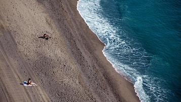 An aerial view of a beach with two people lying on towels, a clear sky, and waves approaching the shore.