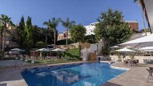 A swimming pool with lounge chairs and umbrellas, surrounded by greenery and buildings. - Hotel Costa Málaga (Adults Recommended) by Pierre & Vacances (Torremolinos)