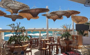 An outdoor seating area with tables and chairs, large woven umbrellas, and a view of the ocean. - Hotel Costa Málaga (Adults Recommended) by Pierre & Vacances (Torremolinos)