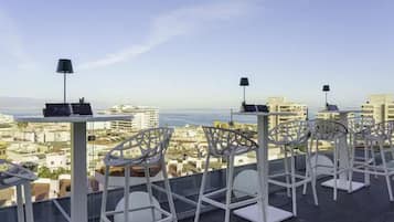 Terraza al aire libre con mesas y sillas, con vistas a un paisaje urbano y al agua.