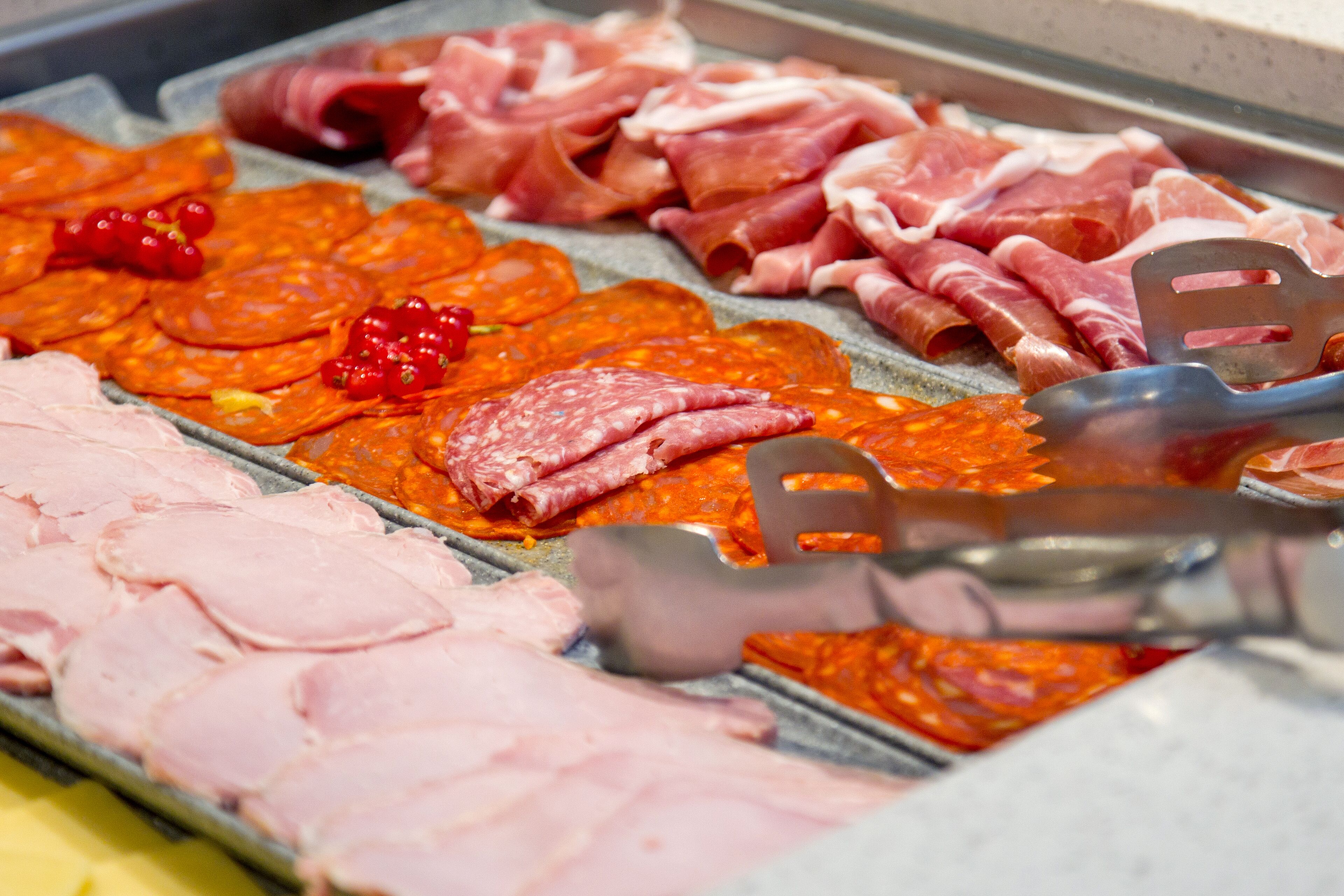 Eine Auswahl an Fleischwaren auf einer Platte, darunter geschnittener Schinken und verschiedene Sorten Salami.
