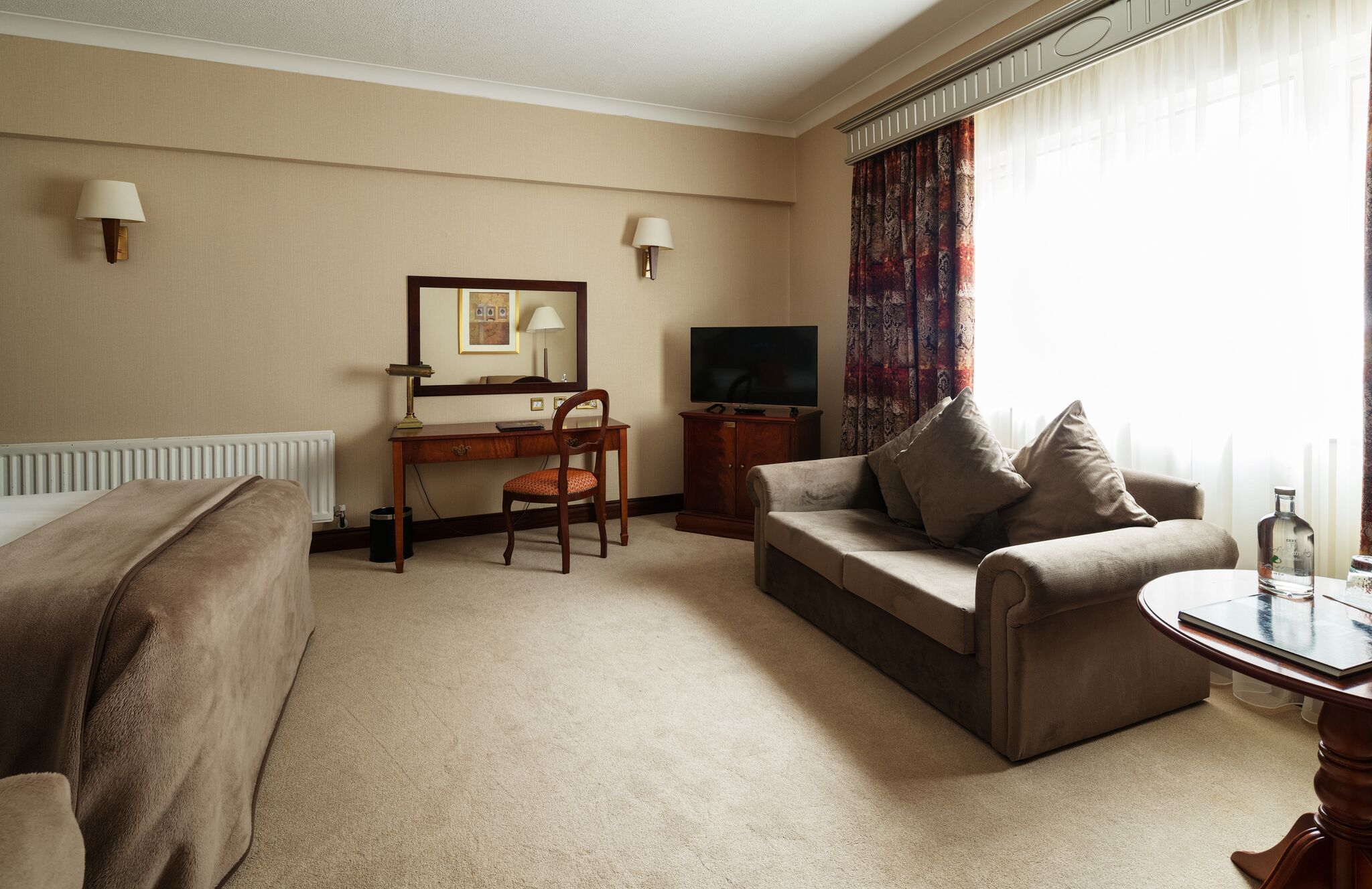 Habitación de hotel con sofá, escritorio con silla, televisión y ventana con cortinas.