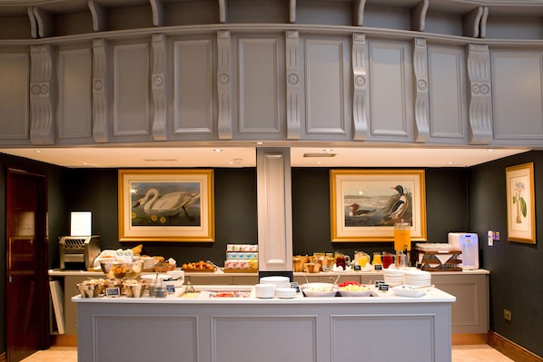 A breakfast buffet with various food items and beverages, framed artwork on the walls, and a modern interior design. - Fitzpatrick Castle Hotel (Dublin)