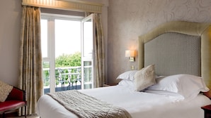 A hotel room with a large bed, a red chair, a balcony with a table, and patterned wallpaper.