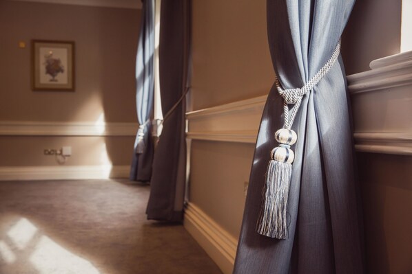 A hallway with a carpeted floor, a framed picture on the wall, and a door with a curtain tied back.