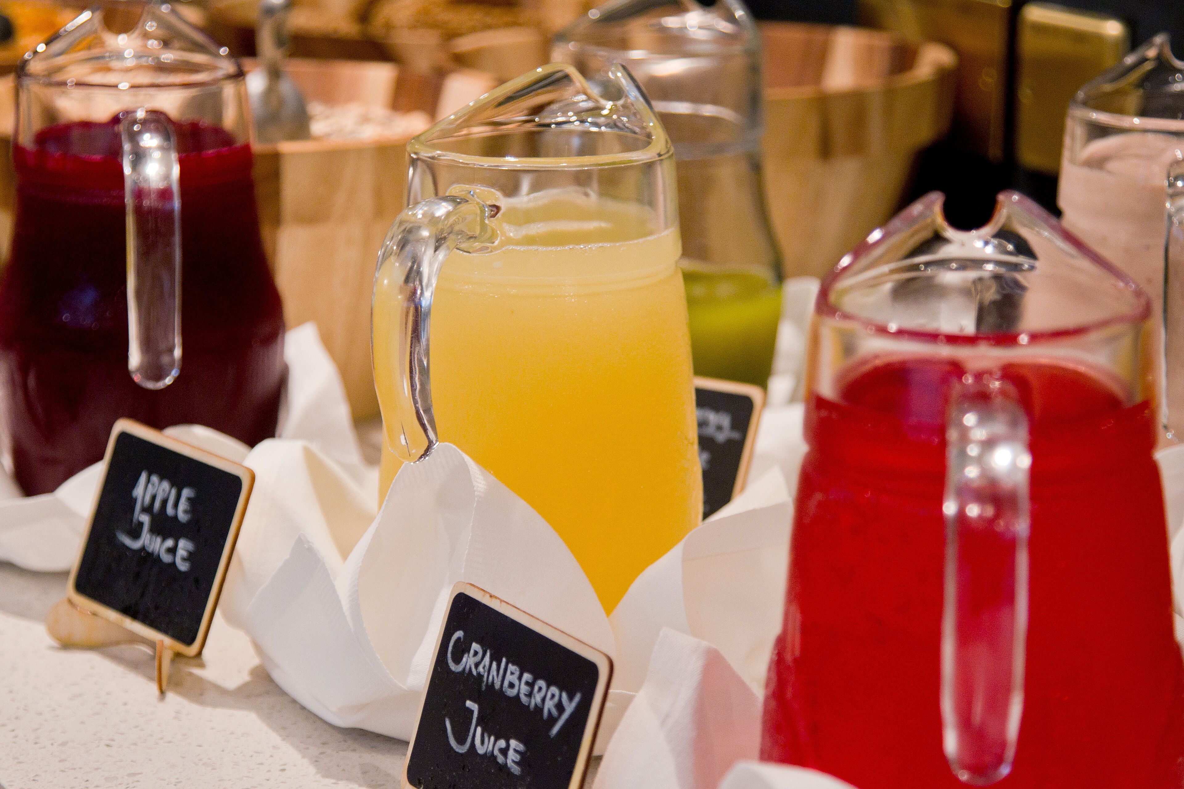 A beverage stand with labeled pitchers of apple juice, cranberry juice, and another unidentified juice.