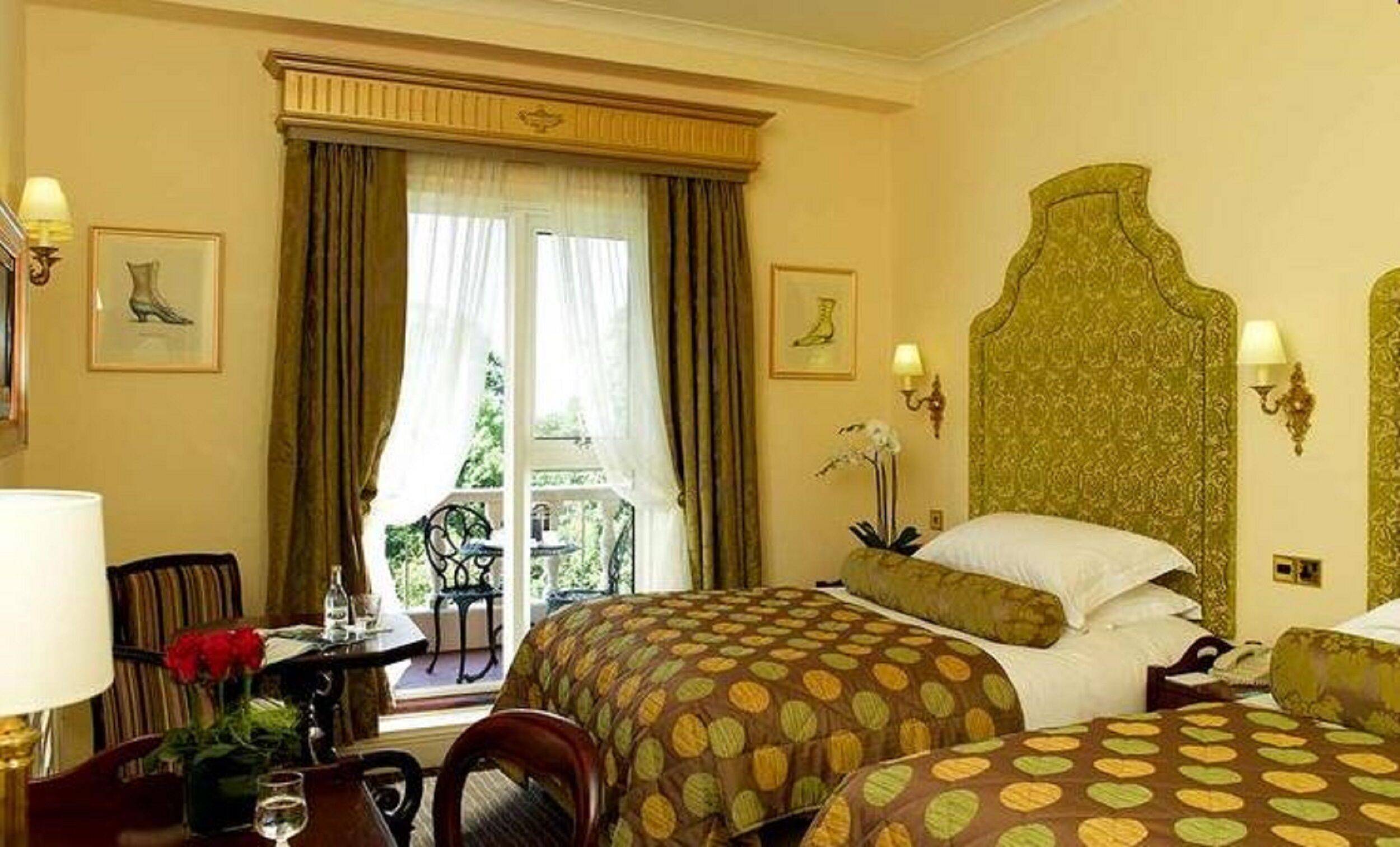 A hotel room with two beds, a dining area, and a view of greenery outside.