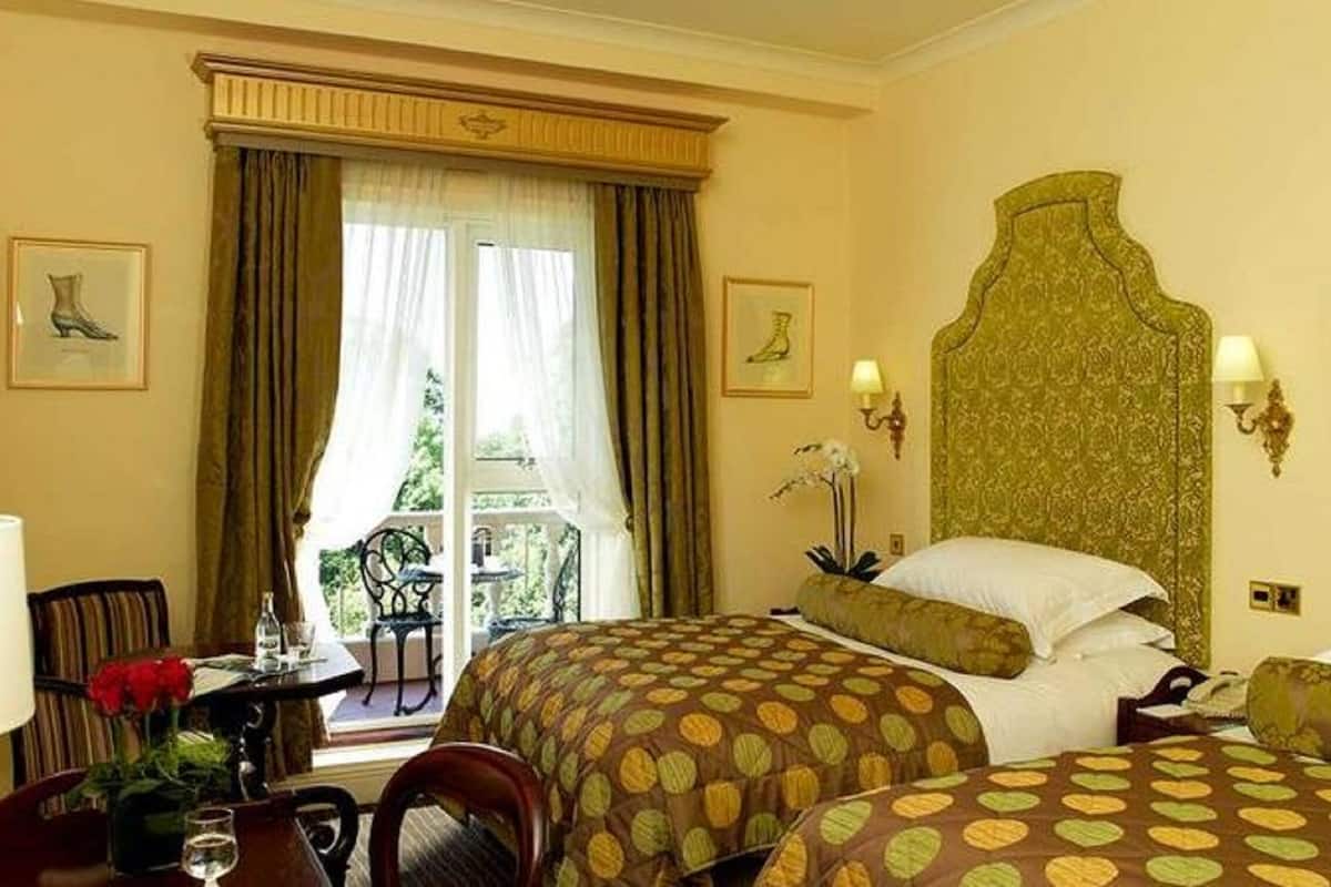A hotel room with two beds, a dining area, and a view of greenery outside.