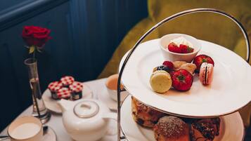 A tea set with a teapot and cups, a rose in a vase, and a tray of pastries and desserts.