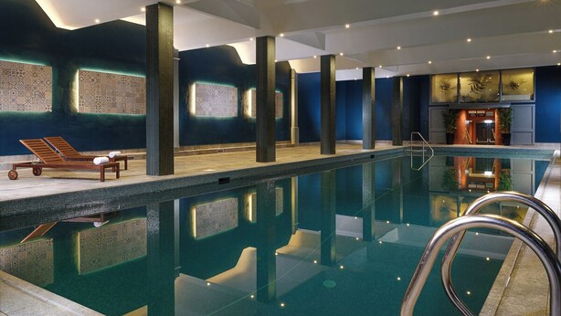 An indoor swimming pool with a clear water surface, lounge chairs, and a well-lit ceiling.
