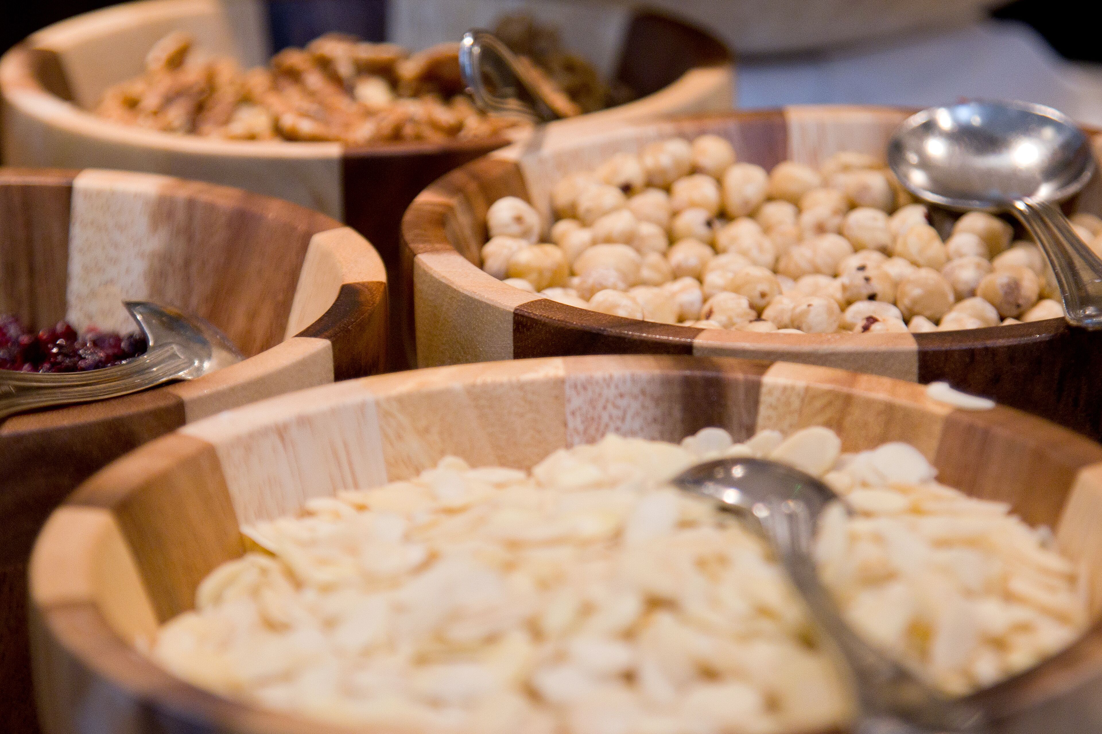 Multiple wooden bowls containing various food items, with spoons placed in some bowls.