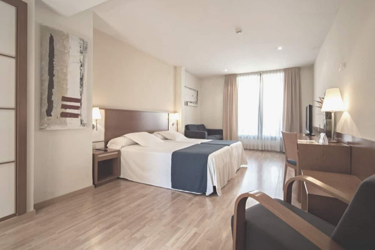 Quarto de hotel com uma cama grande, uma escrivaninha, uma cadeira e uma televisão.