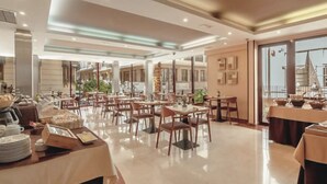 A spacious hotel dining area with multiple tables and chairs, a buffet setup, and large windows offering views of the city. - Hotel RH Sorolla Centro By Hoteles RH (Valencia)