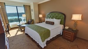 Ein Hotelzimmer mit einem großen Bett, zwei Nachttischen, einem Sessel und Blick auf einen See.