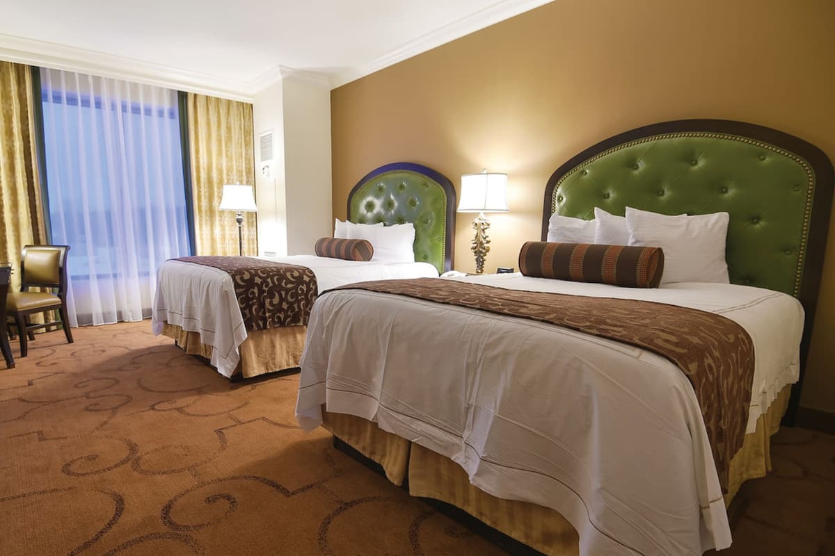 Habitación de hotel con dos camas, una silla y un ventanal grande con cortinas.