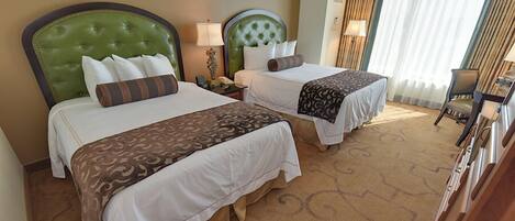 A hotel room with two beds, each with a green headboard, white bedding, and a patterned throw. There is a chair and a lamp on a side table.