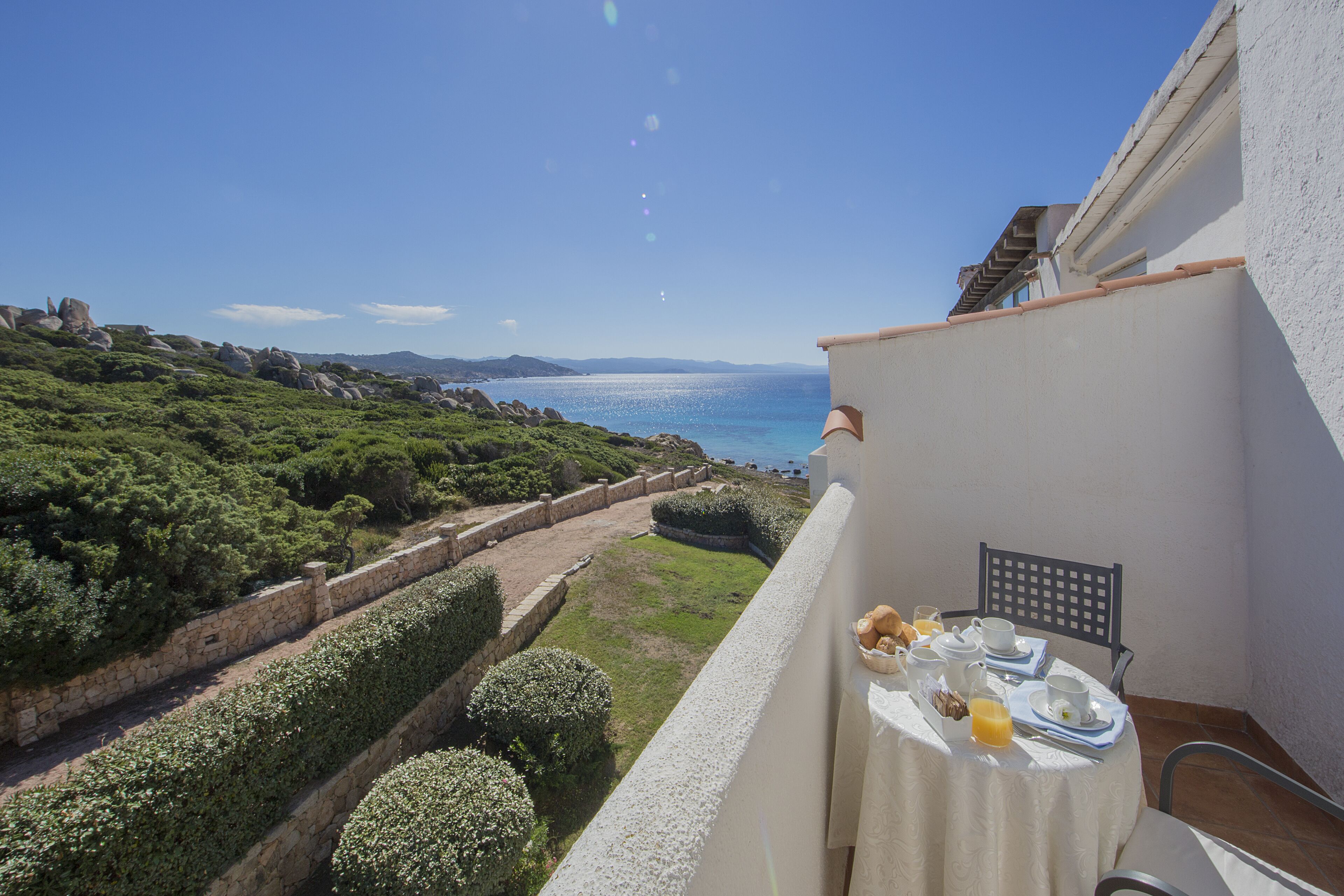 Un balcon avec une table préparée pour le petit-déjeuner, offrant une vue sur un paysage côtier.