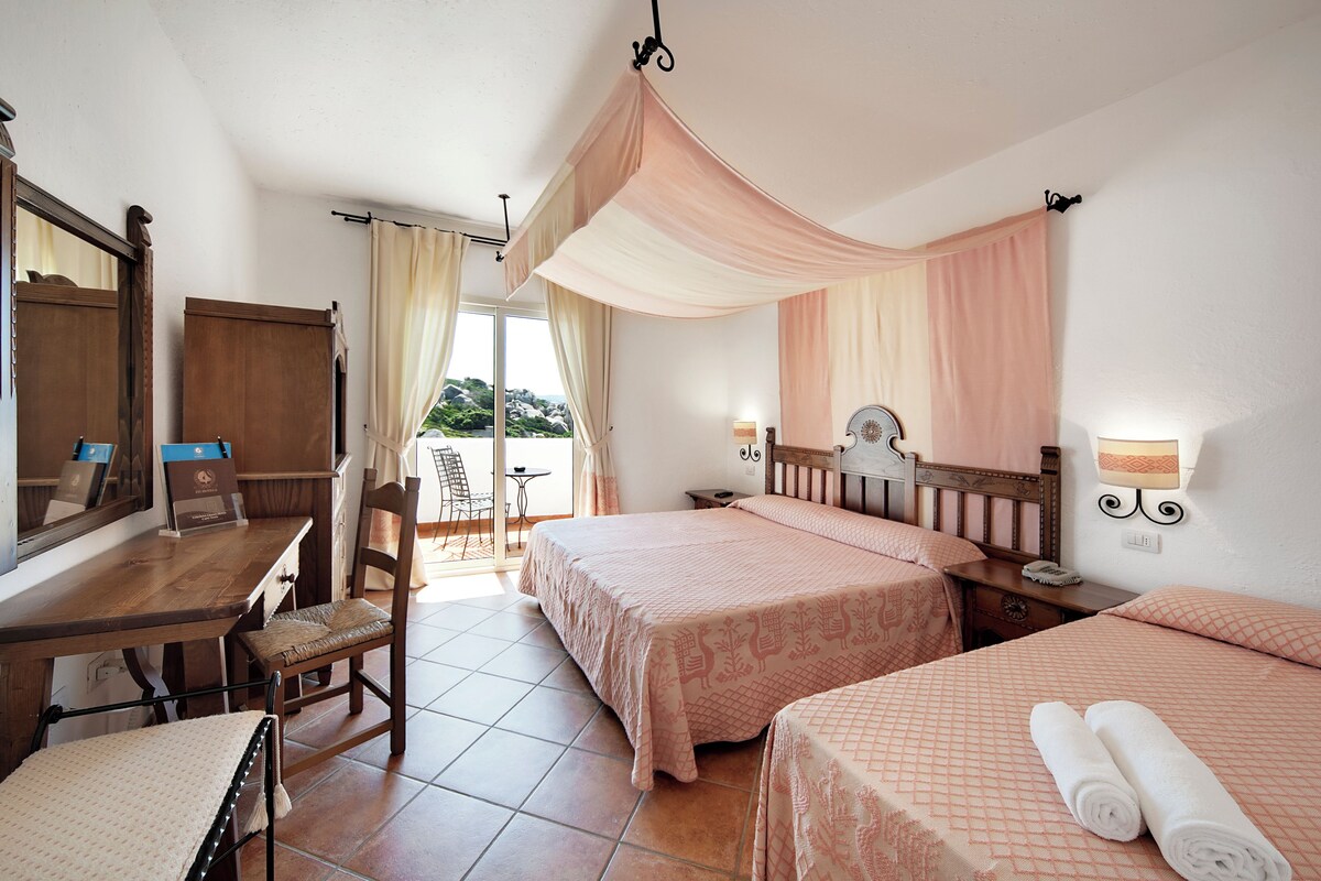 Een hotelkamer met twee bedden, een bureau, een stoel, een spiegel en uitzicht op het groen.
