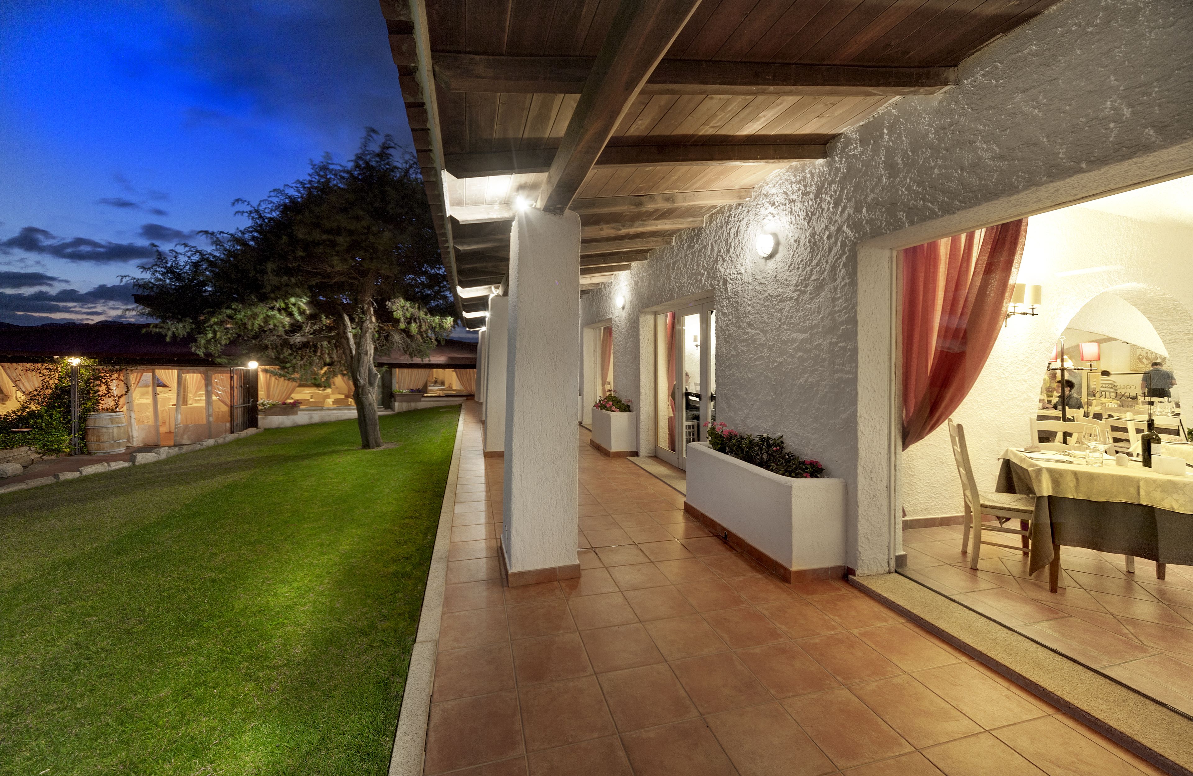 A covered outdoor patio area with a dining table set for two, surrounded by white walls and a wooden ceiling.