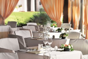 A dining area with tables set for a meal, featuring chairs, plates, cutlery, and wine glasses.