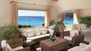 Amplia sala de estar con mobiliario de mimbre, un ventanal con vistas al mar y una planta en maceta.