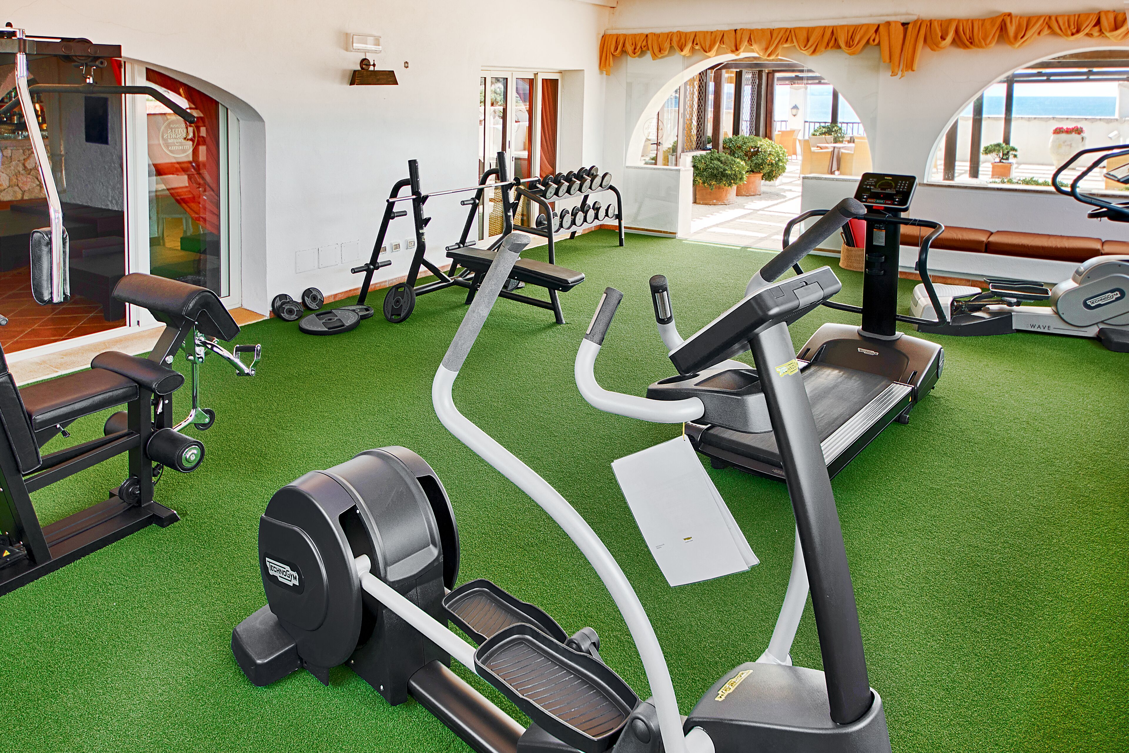 Ein Fitnessstudio mit Laufbändern, Crosstrainern und Gewichten auf Kunstrasen.