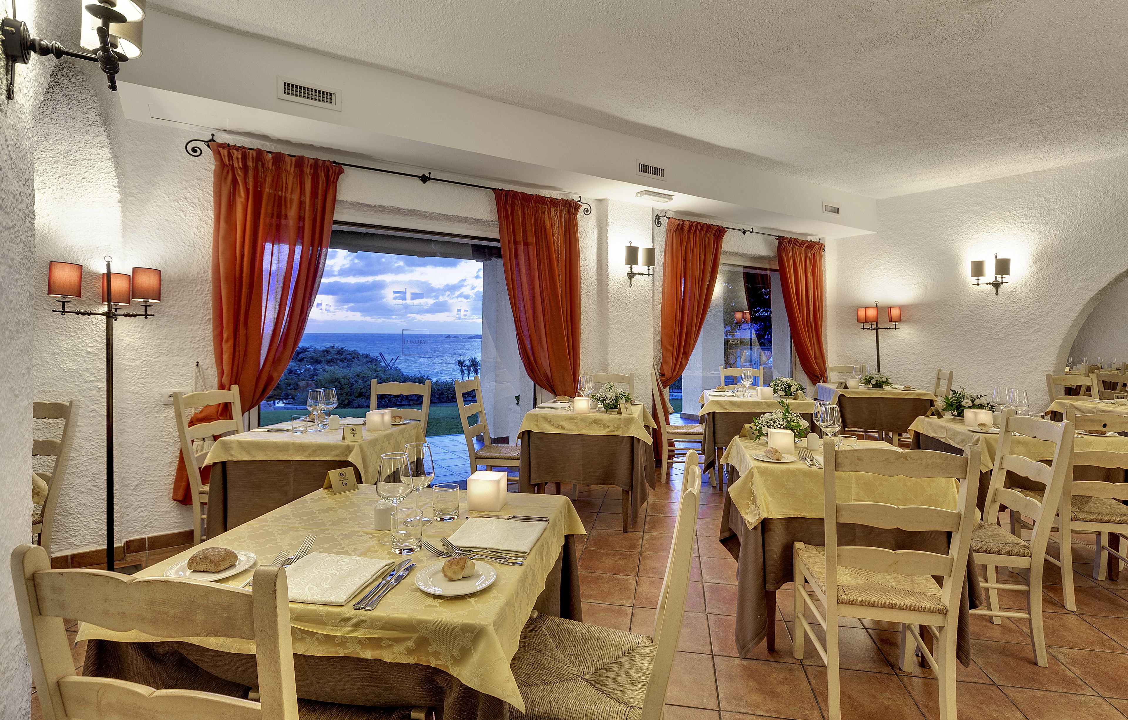 A dining area with tables set for meals, chairs, and a view of the sea.