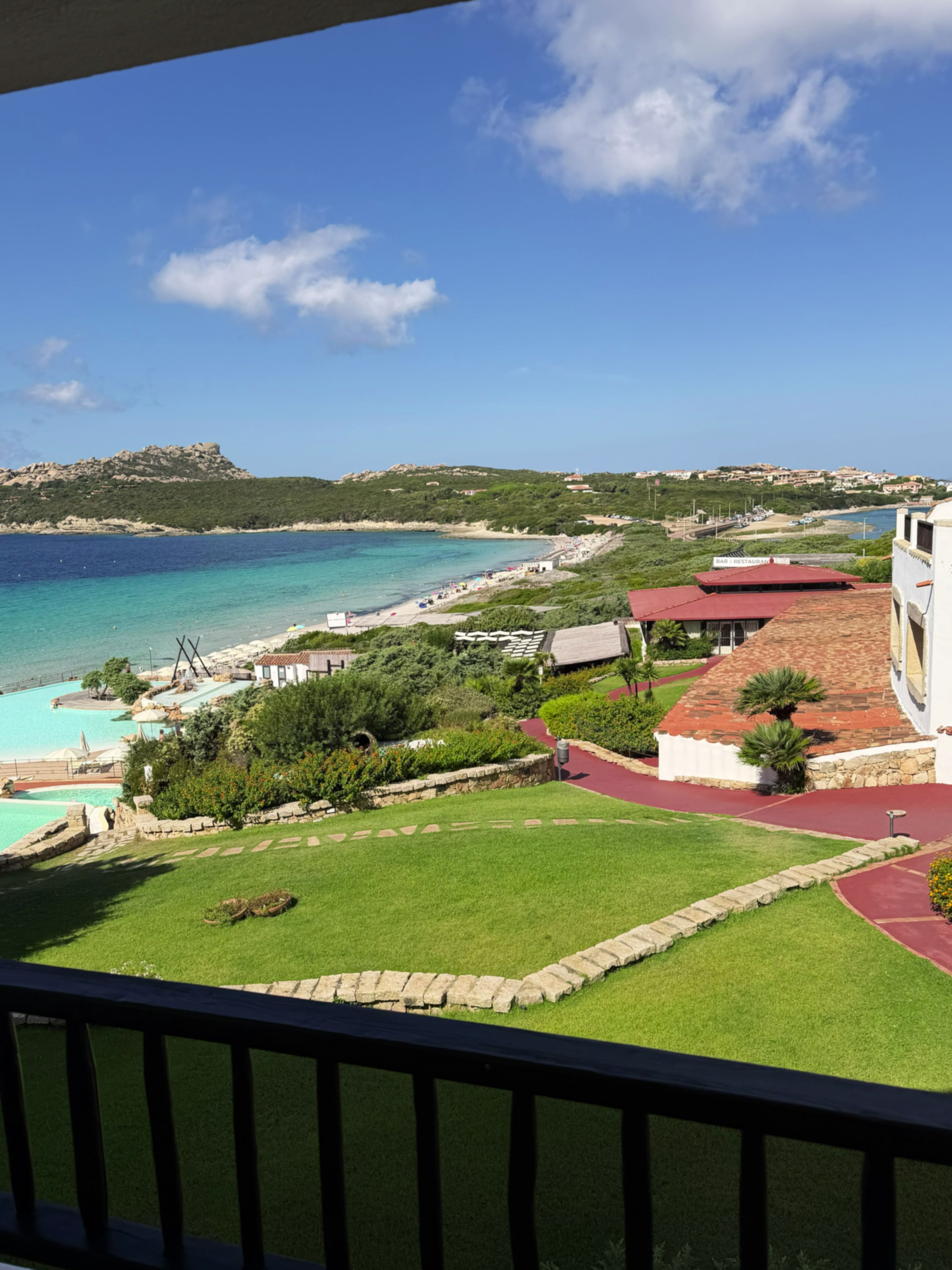 A coastal view with a clear sky, a beach, and a building with a red roof.