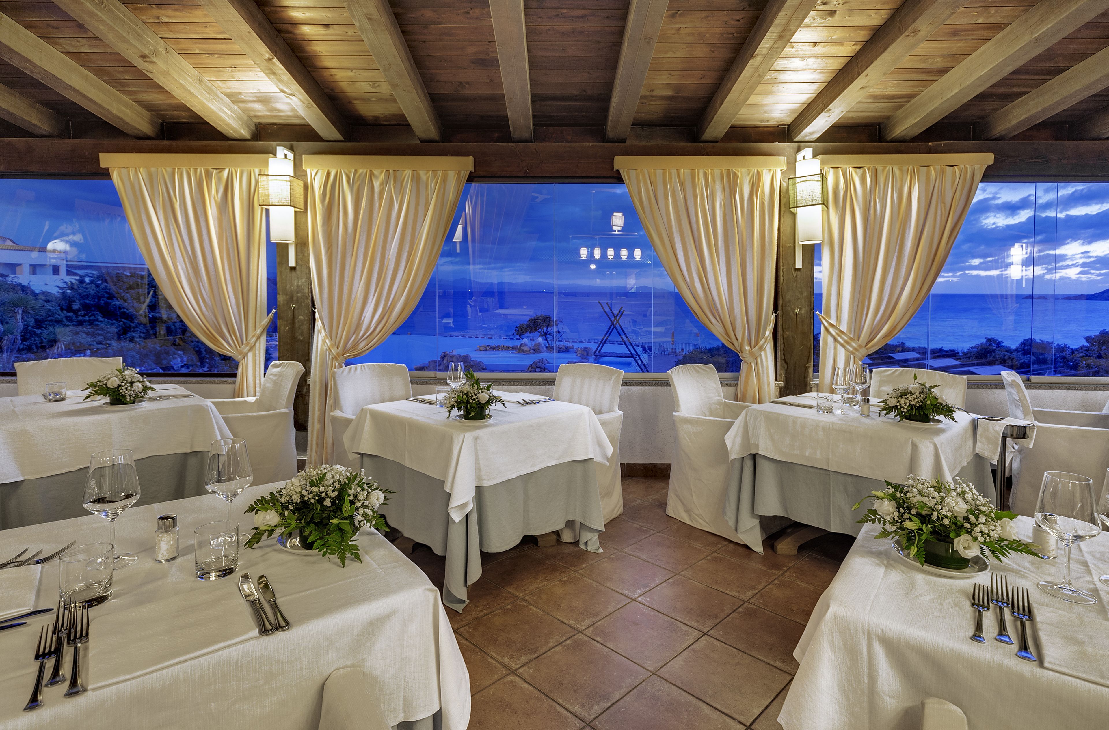 A restaurant with tables set for dining, featuring a view of the sea and a building in the background.