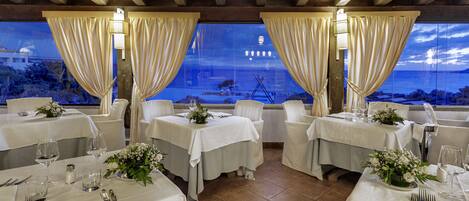 A restaurant with tables set for dining, featuring a view of the sea and a building in the background.