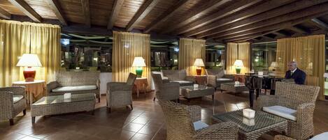 A spacious lobby with wicker furniture, a grand piano, and large windows with curtains.