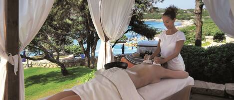 A massage therapy session in a covered outdoor area with a view of the sea and greenery.