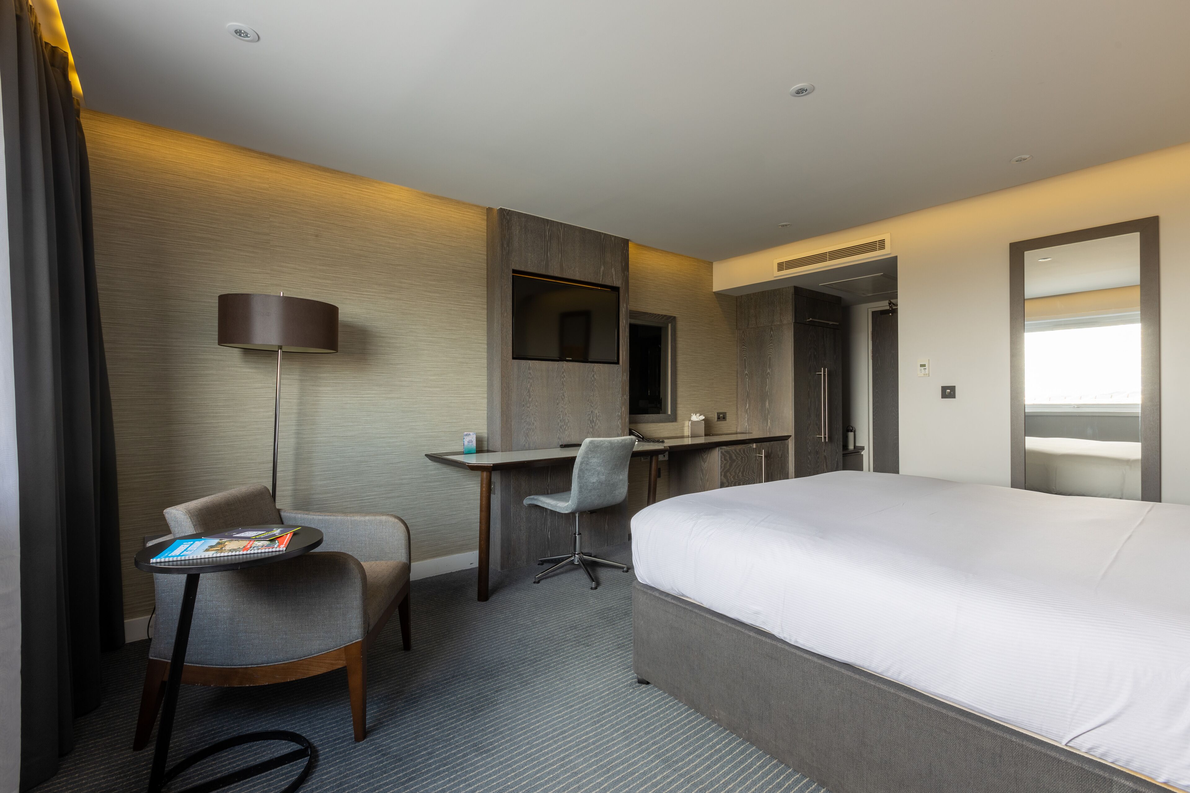 Habitación de hotel con una cama grande, un escritorio con silla, una lámpara y un televisor.