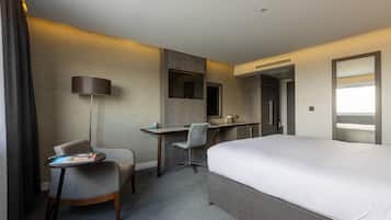 Habitación de hotel con una cama grande, un escritorio con silla, una lámpara y un televisor.