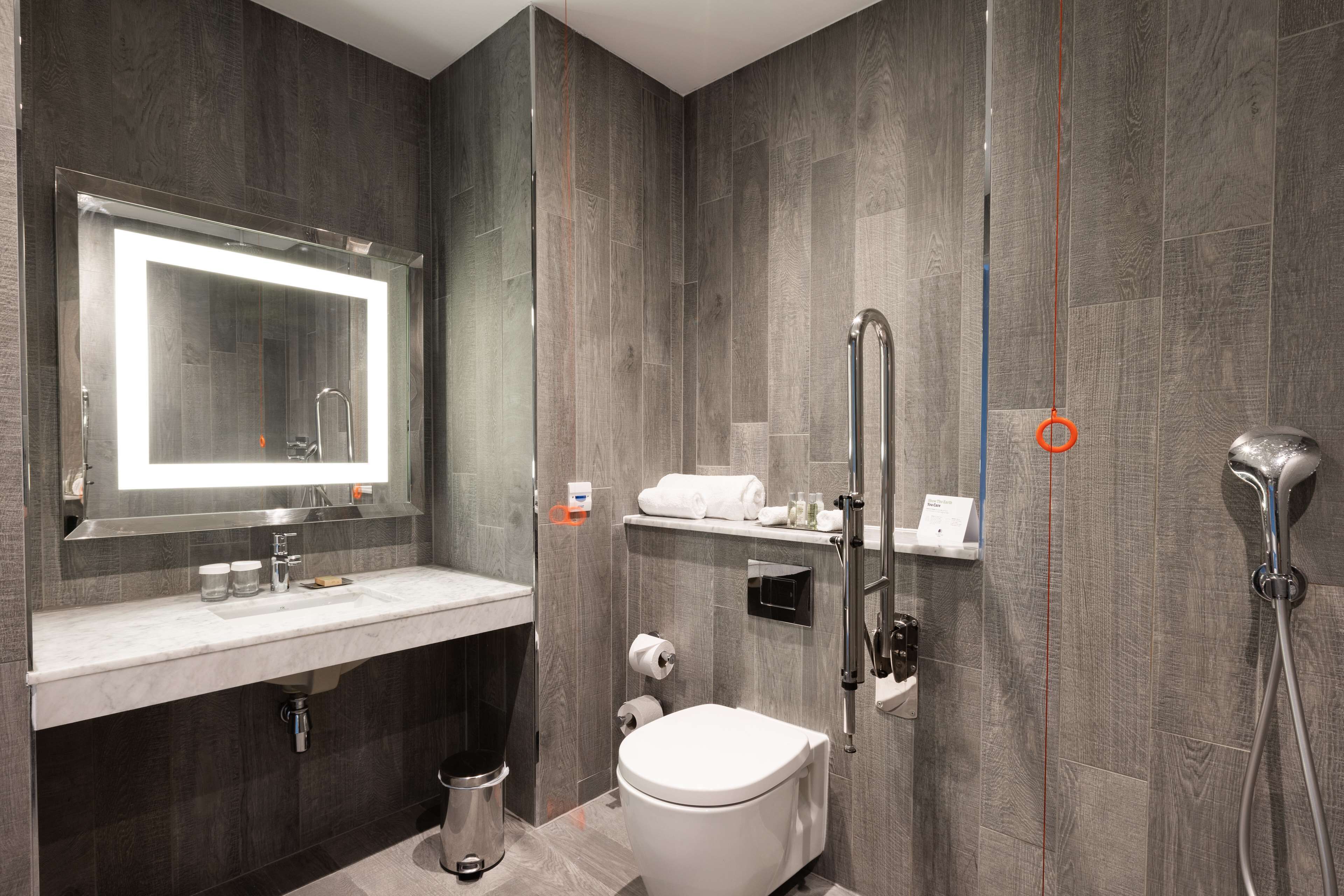 Un baño moderno con un espejo grande, un inodoro, un lavamanos y una ducha.