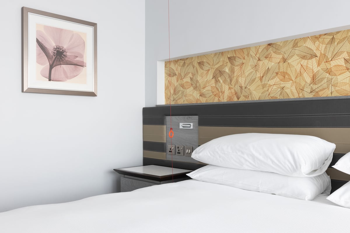 A hotel room with a bed, a nightstand, a wall-mounted power outlet, and a framed picture of a flower.