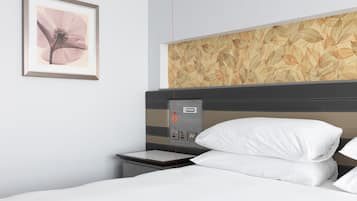 Une chambre d’hôtel comprenant un lit, une table de chevet, une prise de courant fixée au mur et un tableau représentant une fleur.