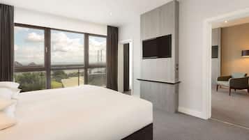 A modern hotel room with a large bed, a TV mounted on the wall, and a view of a bridge and landscape through large windows.