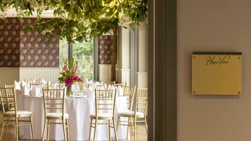Un salón de banquetes con mesas redondas dispuestas para un evento formal, con manteles blancos y sillas doradas.