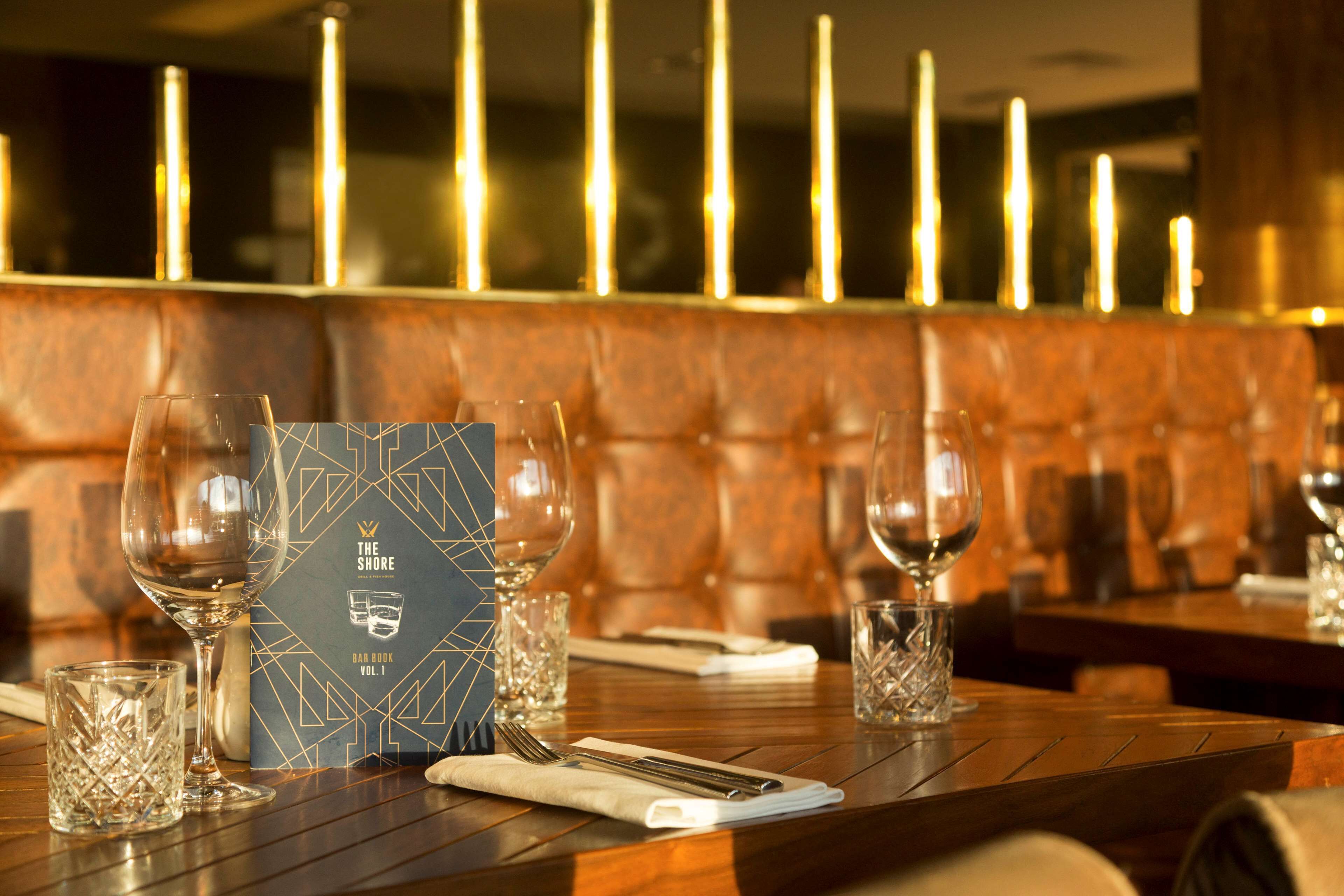 A restaurant setting with a wooden table, wine glasses, a menu, and candle-lit background.